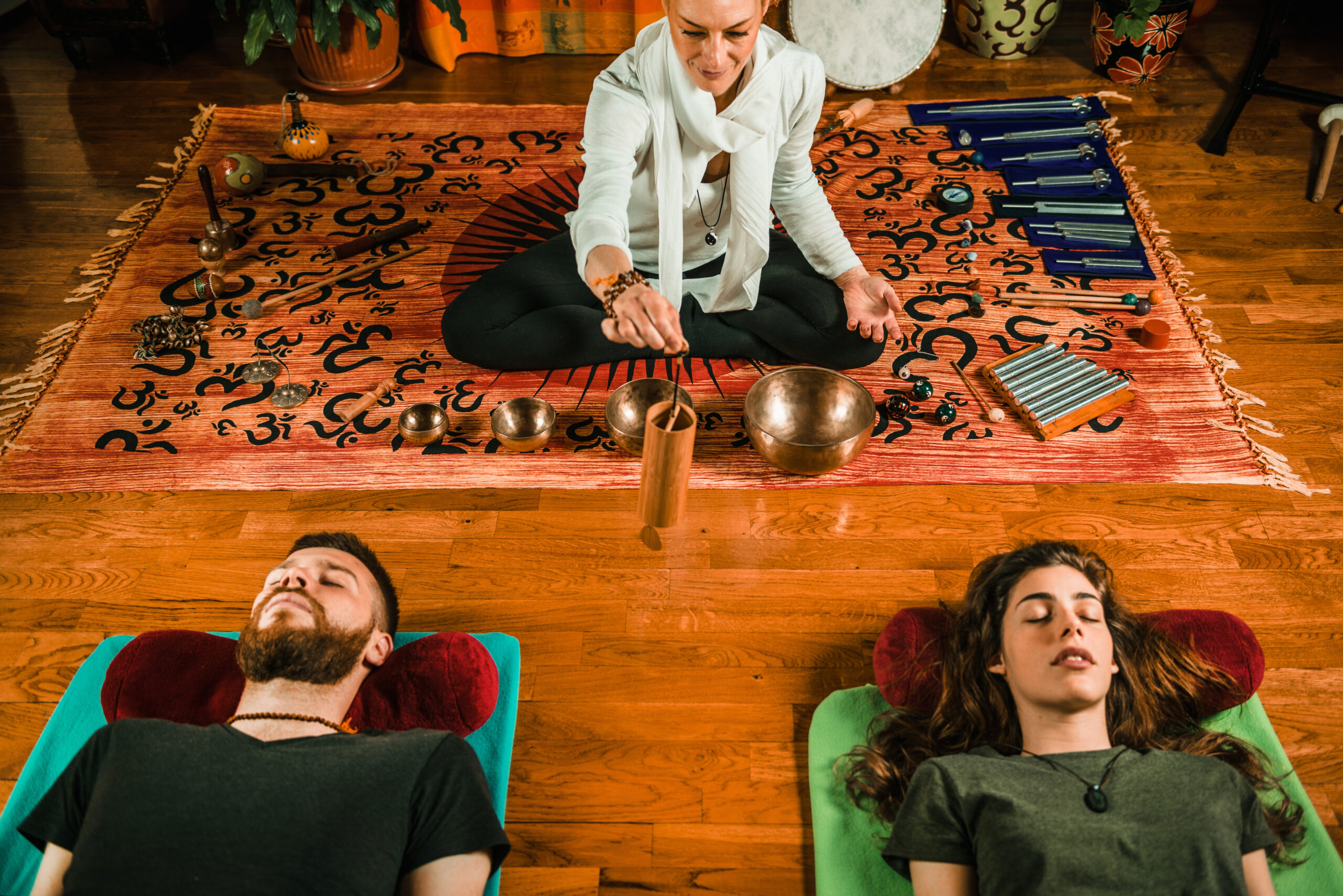 Two people lying in a peaceful sleeping meditation posture, while a third person nearby plays a sound instrument, such as a singing bowl or chimes, creating a calming atmosphere for deep relaxation and conscious dreaming - Koshi chime in sound therapy